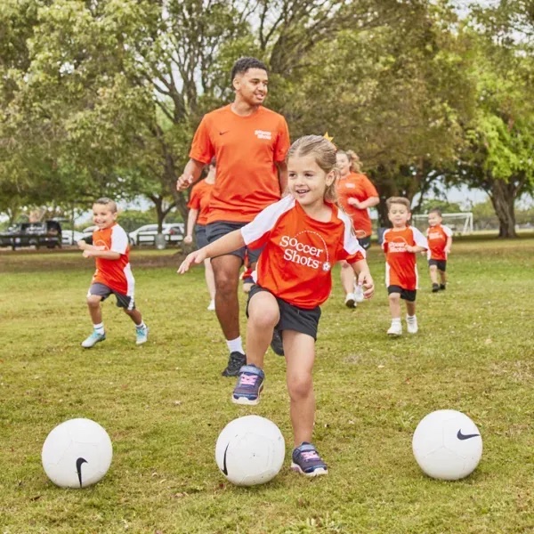 Soccer Shots coach and children running with soccer balls