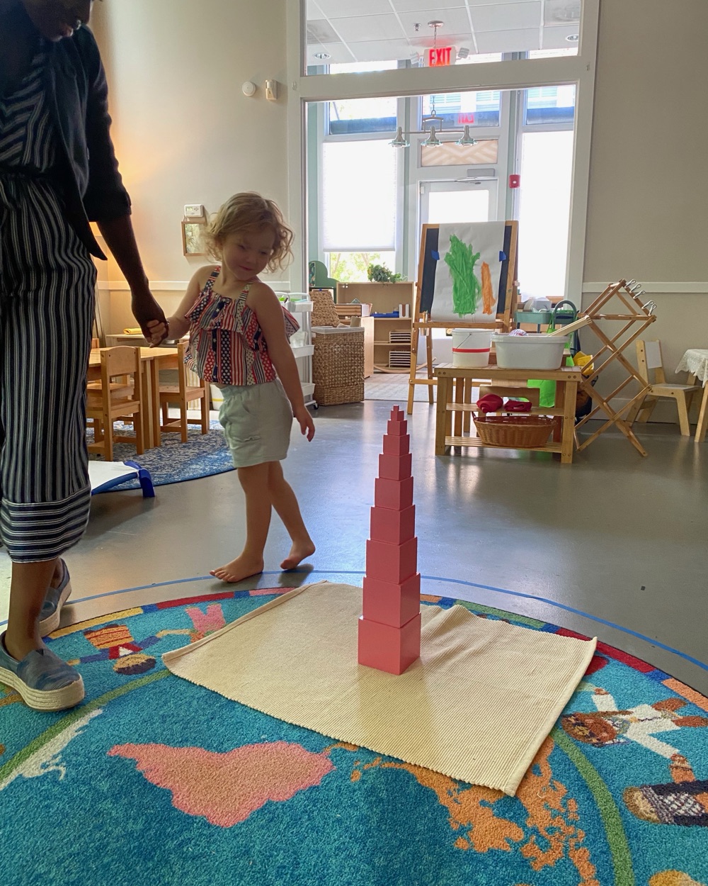 A guide with a young child building the pink tower
